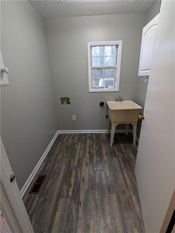 laundry room with dark wood-type flooring, cabinets, and a textured ceiling