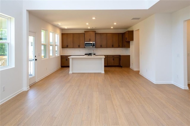 296 River Run Dr, Dallas, GA 30132 - kitchen with stainless steel microwave, light wood-type flooring, backsplash, light countertops, and an island with sink