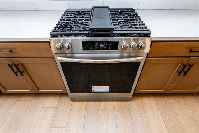 296 River Run Dr, Dallas, GA 30132 - detailed view of stainless steel range with gas stovetop, brown cabinets, light wood-style floors, and tasteful backsplash