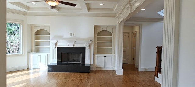 unfurnished living room with wood finished floors, coffered ceiling, a fireplace with raised hearth, ceiling fan, and crown molding