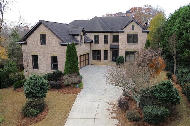 view of front facade with concrete driveway, a garage, brick siding, and a chimney