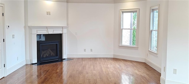 unfurnished living room featuring a fireplace with flush hearth, baseboards, and wood finished floors