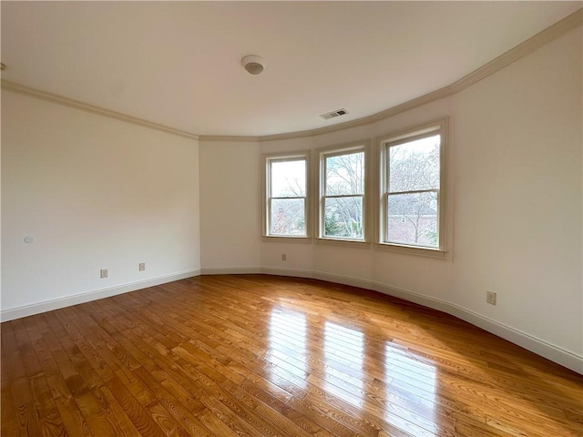 spare room with hardwood / wood-style flooring, crown molding, visible vents, and baseboards