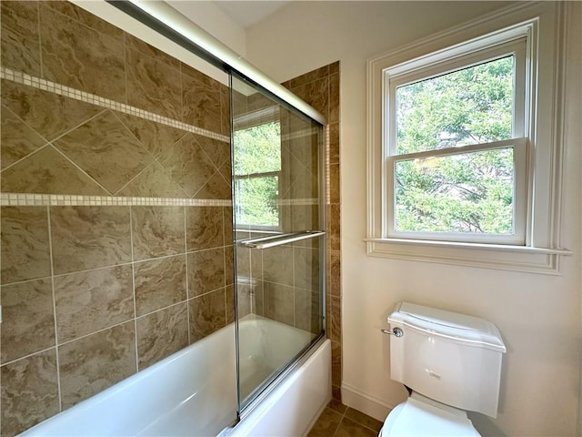 bathroom with tile patterned floors, toilet, baseboards, and bath / shower combo with glass door