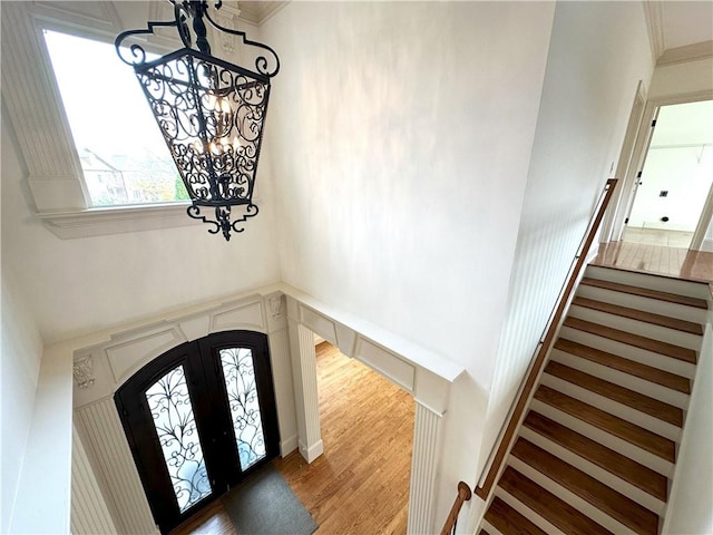 foyer with stairway, light wood finished floors, french doors, crown molding, and a notable chandelier