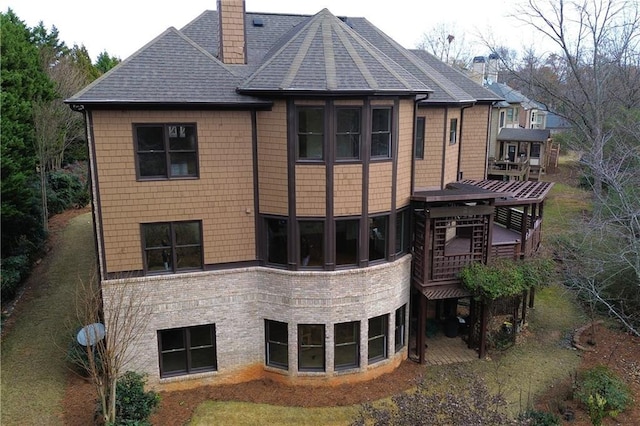 back of house with a shingled roof, a wooden deck, brick siding, and a chimney