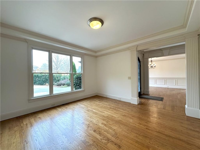 empty room with a notable chandelier, wood finished floors, baseboards, and ornamental molding