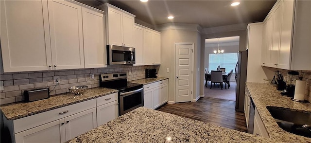 kitchen with dark wood-type flooring, white cabinetry, appliances with stainless steel finishes, light stone countertops, and backsplash