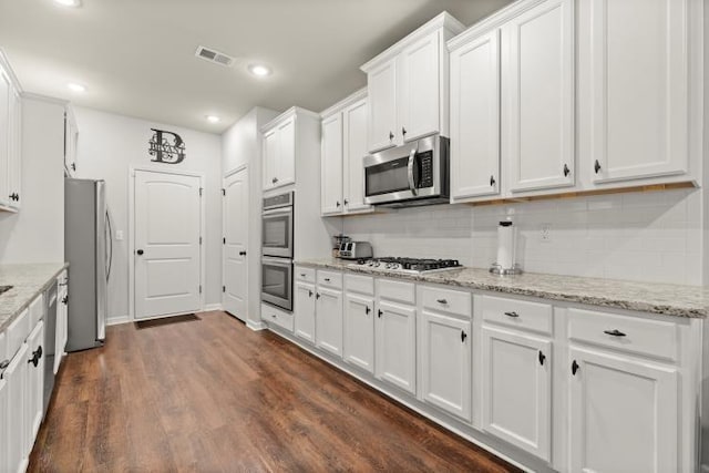 kitchen with dark wood-type flooring, light stone counters, appliances with stainless steel finishes, decorative backsplash, and white cabinets