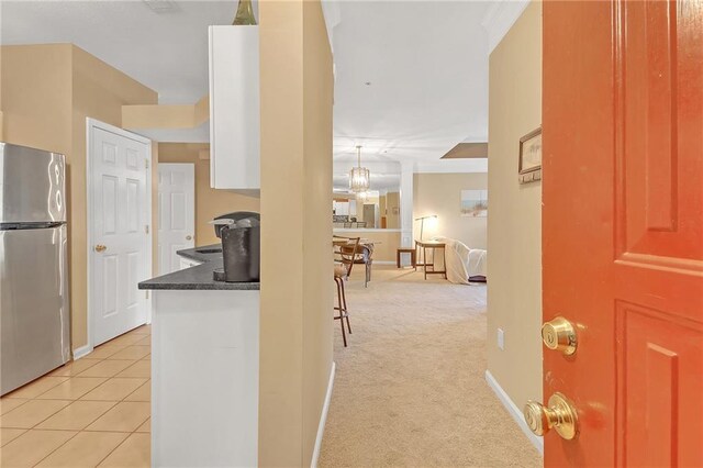 interior space featuring white cabinetry, stainless steel refrigerator, decorative light fixtures, light colored carpet, and a notable chandelier