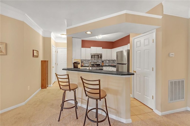 kitchen with tasteful backsplash, white cabinets, light carpet, a kitchen breakfast bar, and appliances with stainless steel finishes