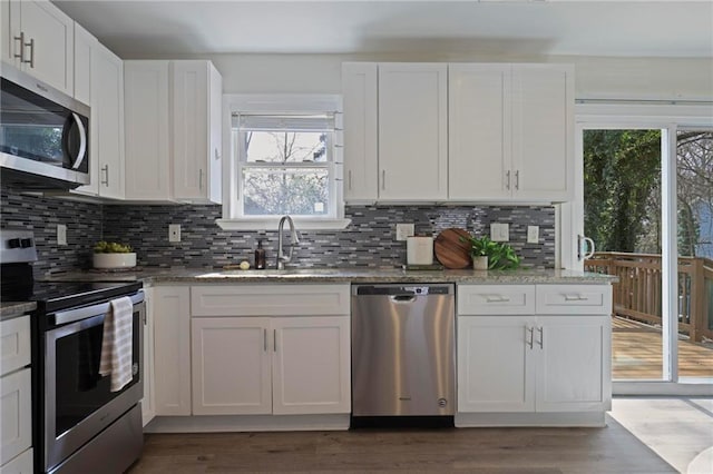 kitchen featuring stainless steel appliances, light stone counters, a sink, and white cabinetry