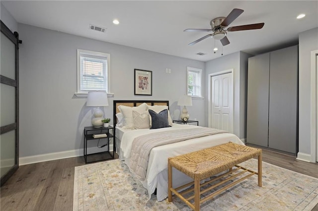 bedroom featuring a barn door, multiple windows, wood finished floors, and visible vents