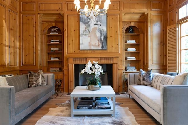 living room featuring light wood-type flooring, built in shelves, wooden walls, and an inviting chandelier