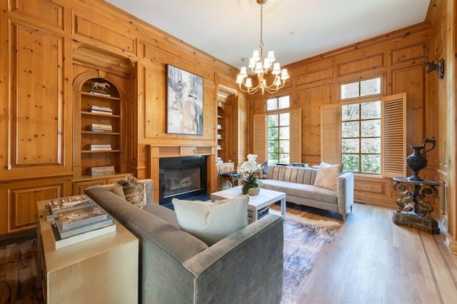 living room with built in features, wooden walls, a notable chandelier, and hardwood / wood-style floors