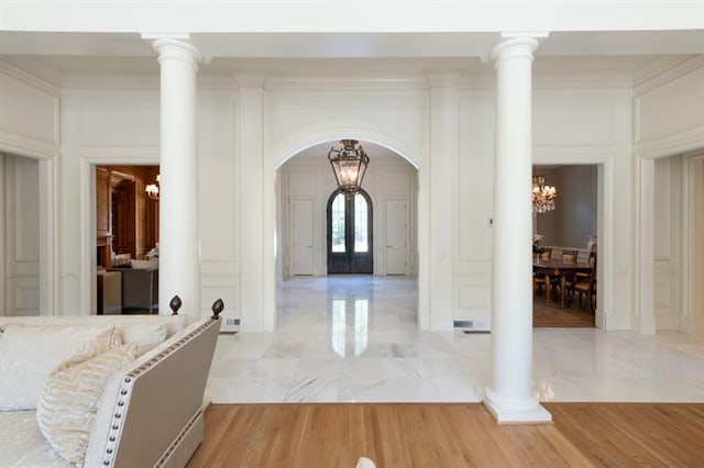 foyer featuring crown molding, ornate columns, and an inviting chandelier