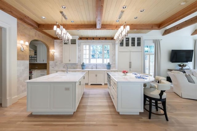 kitchen featuring white cabinets, hanging light fixtures, a kitchen island with sink, and decorative backsplash