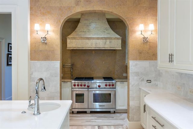 kitchen featuring custom exhaust hood, sink, range with two ovens, and tasteful backsplash