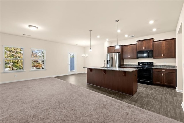 kitchen with hanging light fixtures, dark colored carpet, an island with sink, a kitchen bar, and black appliances