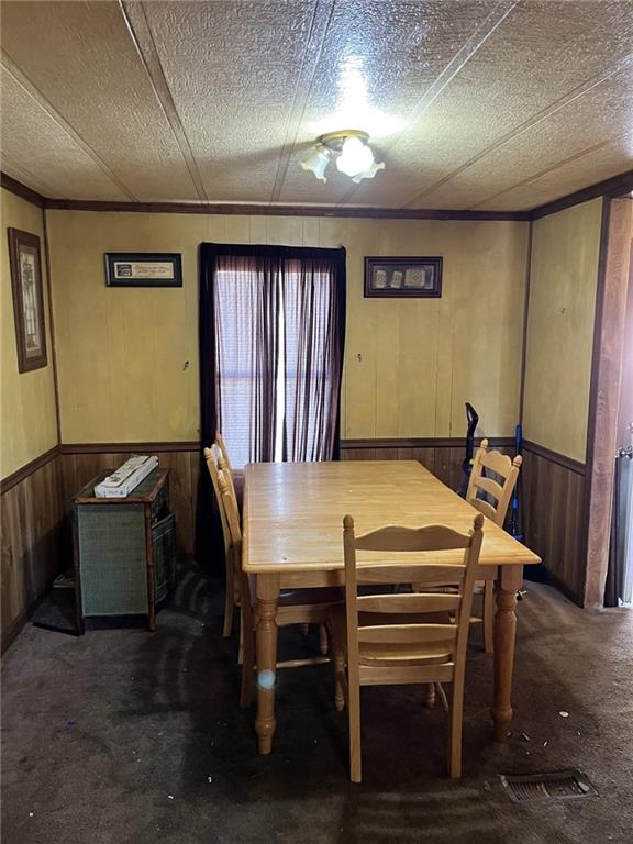 carpeted dining space featuring a textured ceiling and wood walls