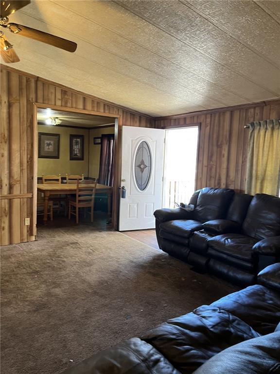 carpeted living room featuring wooden walls and ceiling fan