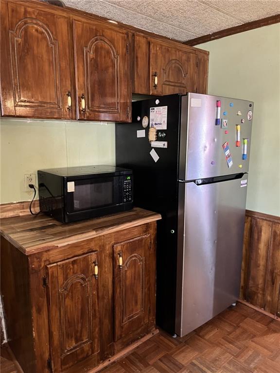 kitchen with butcher block counters, stainless steel refrigerator, ornamental molding, wooden walls, and dark parquet floors