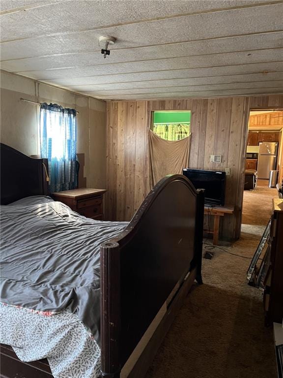 carpeted bedroom featuring stainless steel refrigerator and wood walls