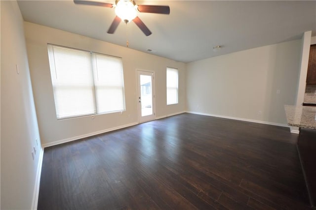 unfurnished living room featuring ceiling fan, dark wood-type flooring, and a wealth of natural light