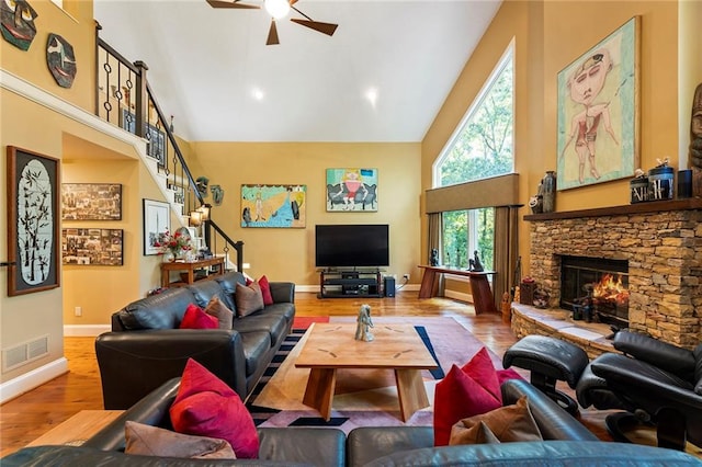 living room featuring ceiling fan, a stone fireplace, wood-type flooring, and high vaulted ceiling