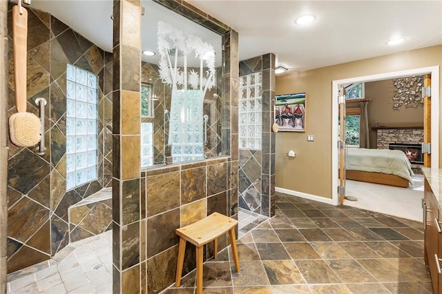 bathroom with a tile shower, a stone fireplace, and plenty of natural light