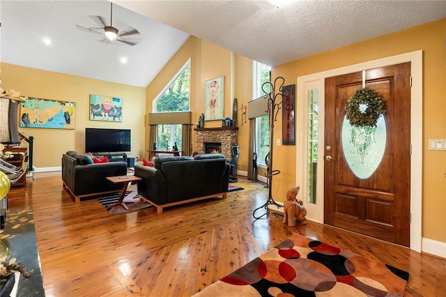 entryway featuring a textured ceiling, ceiling fan, high vaulted ceiling, a fireplace, and hardwood / wood-style floors