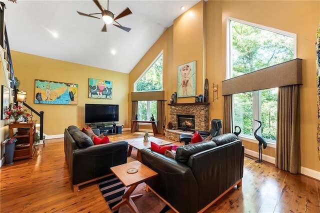 living room featuring light hardwood / wood-style flooring, high vaulted ceiling, a healthy amount of sunlight, and a stone fireplace