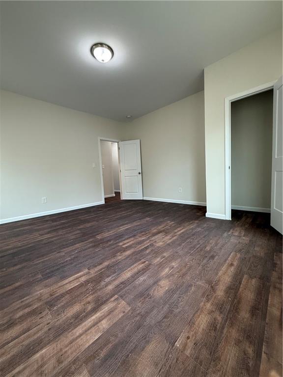 empty room with baseboards and dark wood-type flooring