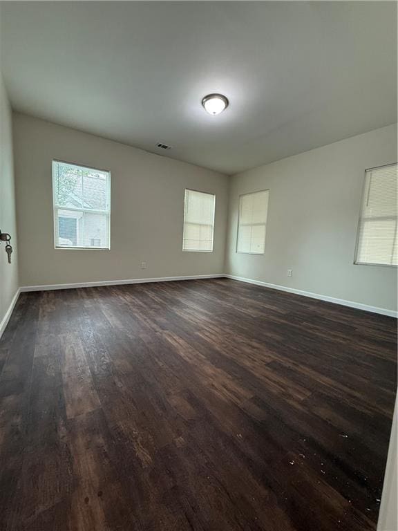 spare room featuring baseboards, visible vents, a wealth of natural light, and dark wood-style flooring