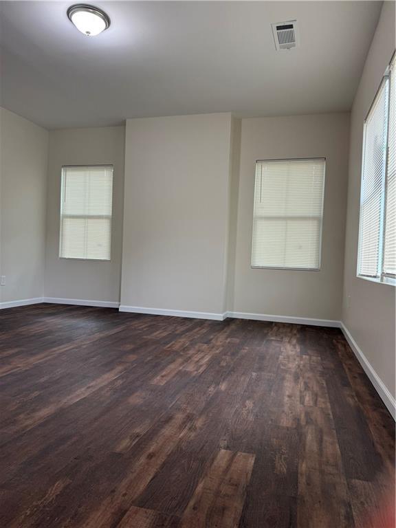 empty room featuring baseboards, visible vents, and dark wood-type flooring