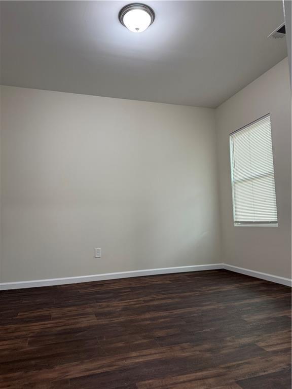 empty room with baseboards, dark wood-type flooring, and visible vents