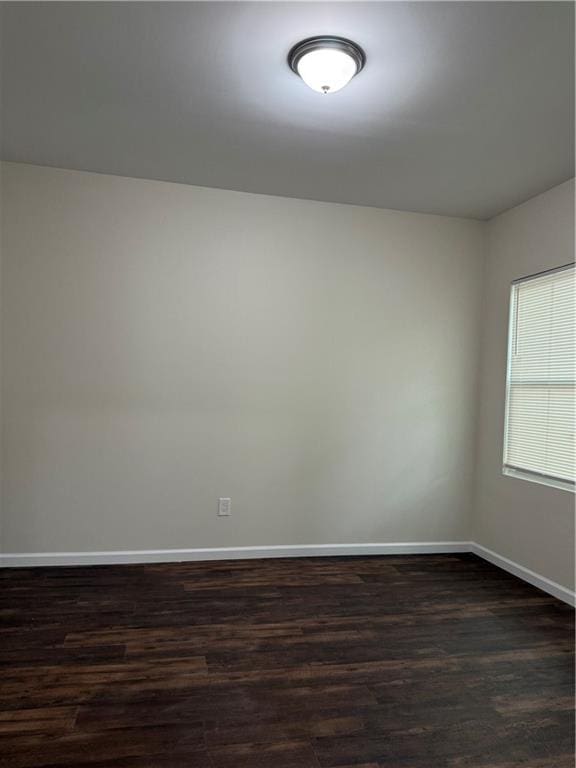 spare room featuring dark wood-type flooring and baseboards