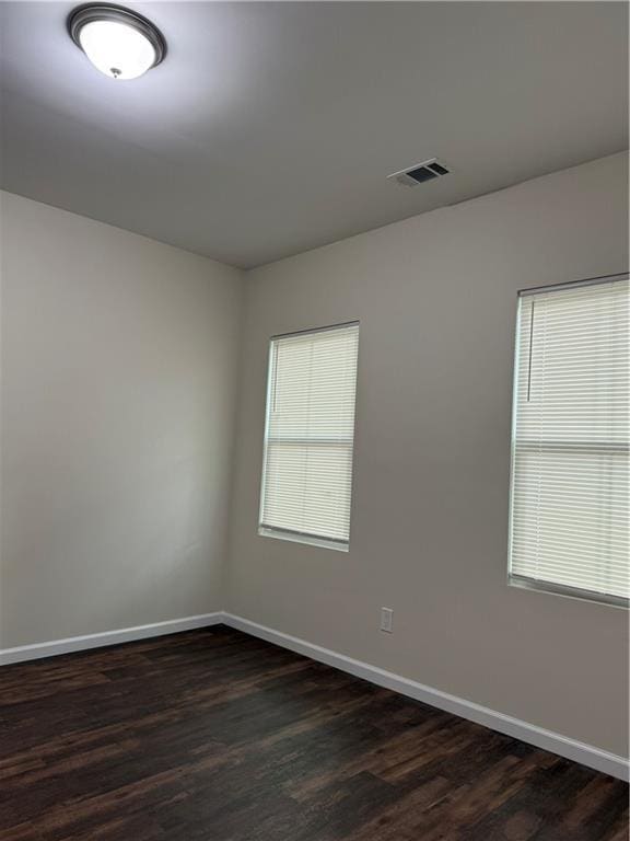 spare room with dark wood-type flooring, visible vents, and baseboards