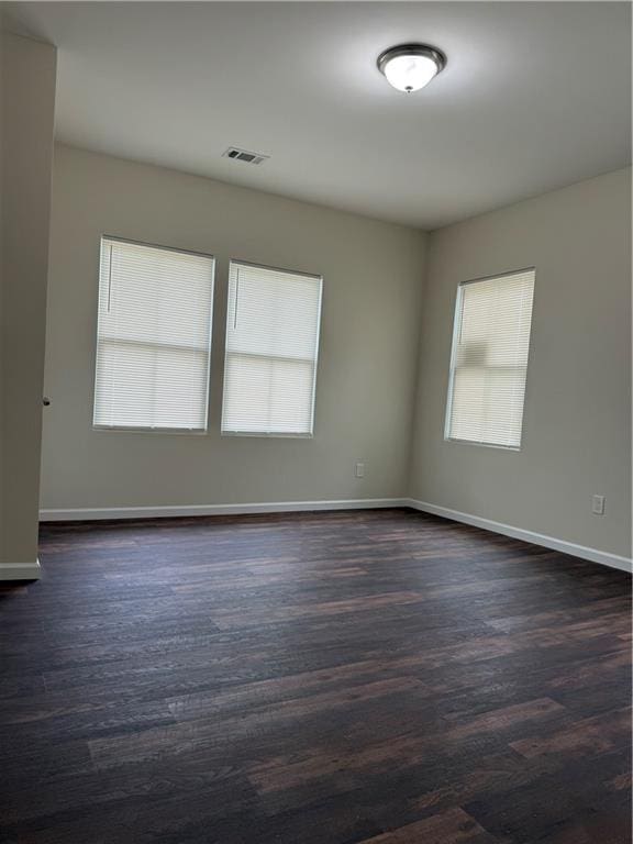 spare room with visible vents, baseboards, and dark wood-type flooring