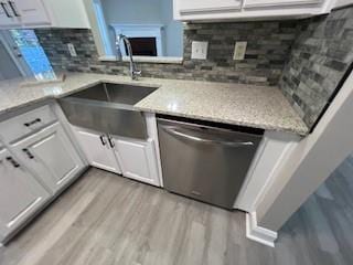 kitchen with sink, light hardwood / wood-style flooring, stainless steel dishwasher, light stone countertops, and white cabinetry