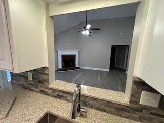 kitchen featuring lofted ceiling, dark wood-type flooring, sink, ceiling fan, and light stone counters