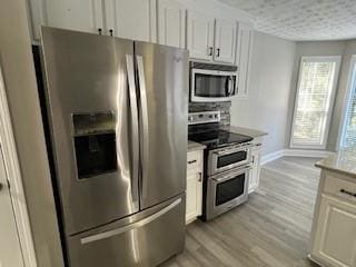 kitchen featuring a textured ceiling, white cabinetry, stainless steel appliances, and light hardwood / wood-style flooring