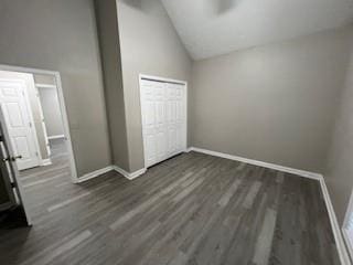 unfurnished bedroom with dark hardwood / wood-style floors, high vaulted ceiling, and a closet