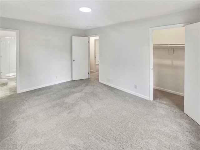 unfurnished bedroom featuring light carpet, ensuite bath, and a spacious closet