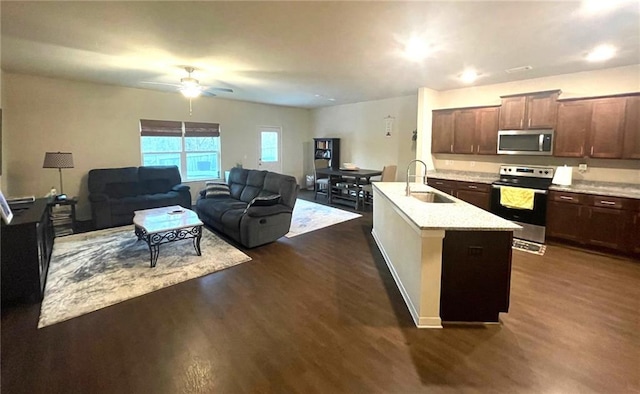 kitchen with a sink, open floor plan, appliances with stainless steel finishes, dark wood-style floors, and a center island with sink