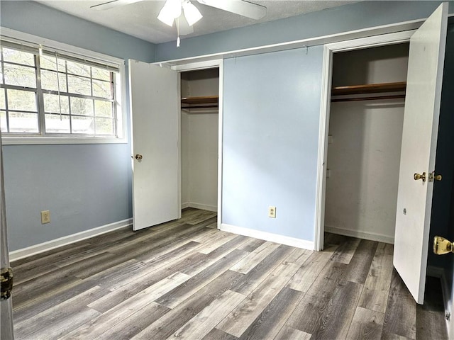 unfurnished bedroom with dark wood-type flooring, ceiling fan, and multiple closets