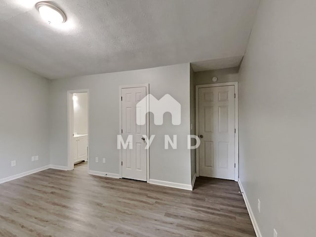 unfurnished bedroom with ensuite bath, wood finished floors, baseboards, and a textured ceiling