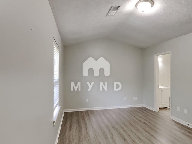 empty room featuring lofted ceiling, a textured ceiling, baseboards, visible vents, and wood finished floors