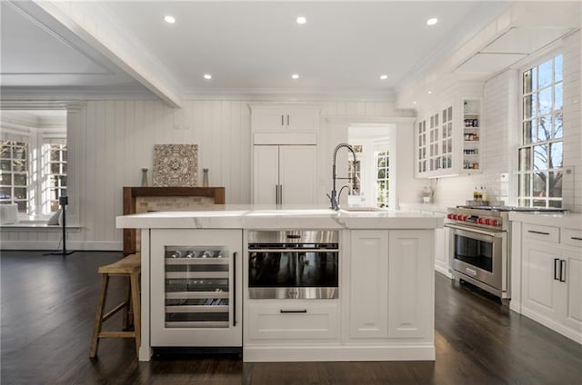 kitchen featuring an island with sink, dark hardwood / wood-style floors, high end appliances, beverage cooler, and white cabinets