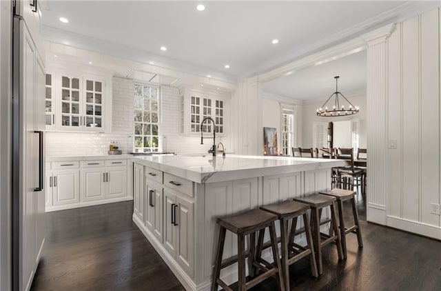 kitchen featuring backsplash, dark hardwood / wood-style floors, crown molding, a kitchen island with sink, and white cabinets